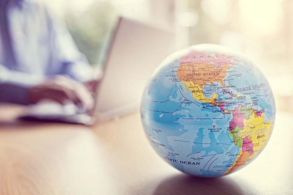 Close-up of a globe with a person using a laptop in the background, representing how Mocean SMS Messaging Campaign solutions empower Indonesian businesses worldwide.